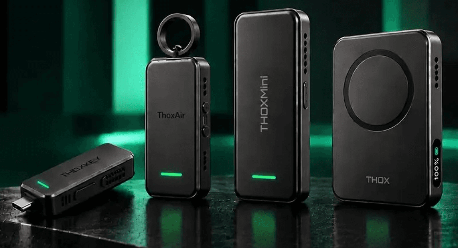 Four THOX devices in Matte Black on a dark stone ledge, lit by vertical green light bars: ThoxKey, a USB-C stick lying flat with a green status bar; ThoxAir, standing upright with its metal attachment ring; ThoxMini, standing upright beside it; and ThoxClip, with a circular magnetic ring on its face and a 100% readout on its side.